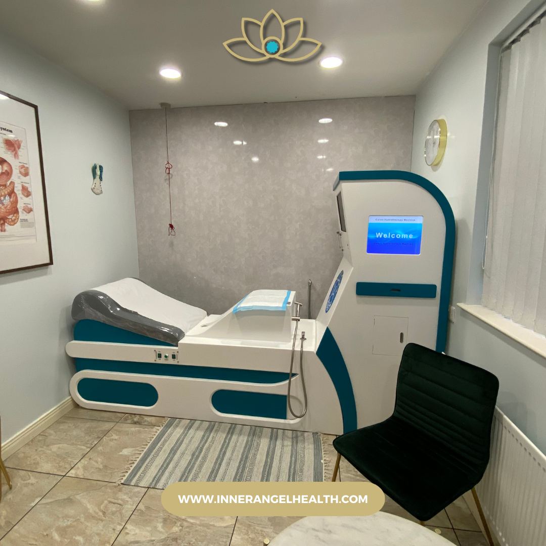 Modern colonic hydrotherapy treatment room at Inner Angel Health, featuring the IA open system device with a padded treatment bed, overhead lighting, digestive anatomy wall chart, and clean, calming decor.